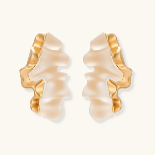 Sculptural wave-textured statement earrings with flowing organic ridges in metallic finish on cream background